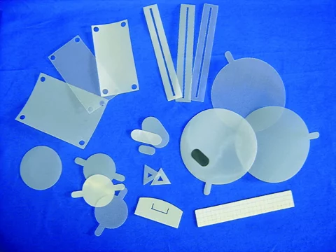 Verschiedene per Laser zugeschnittene Kunststoff-Filterteile in diversen geometrischen Formen auf blauem Untergrund.